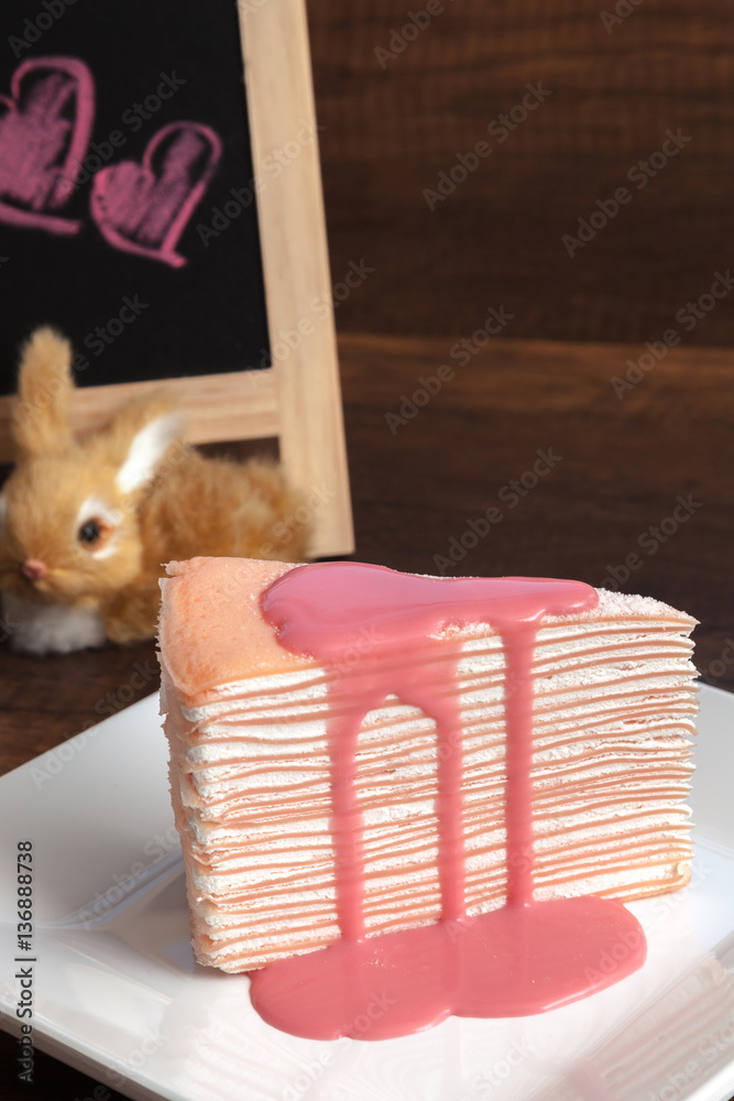 Pink crepe cake with pink custard sauce on wooden table