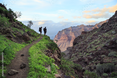 Silhouette of two people with bagpacks enjoying the views while trekking Gran Canaria Island, Spain.