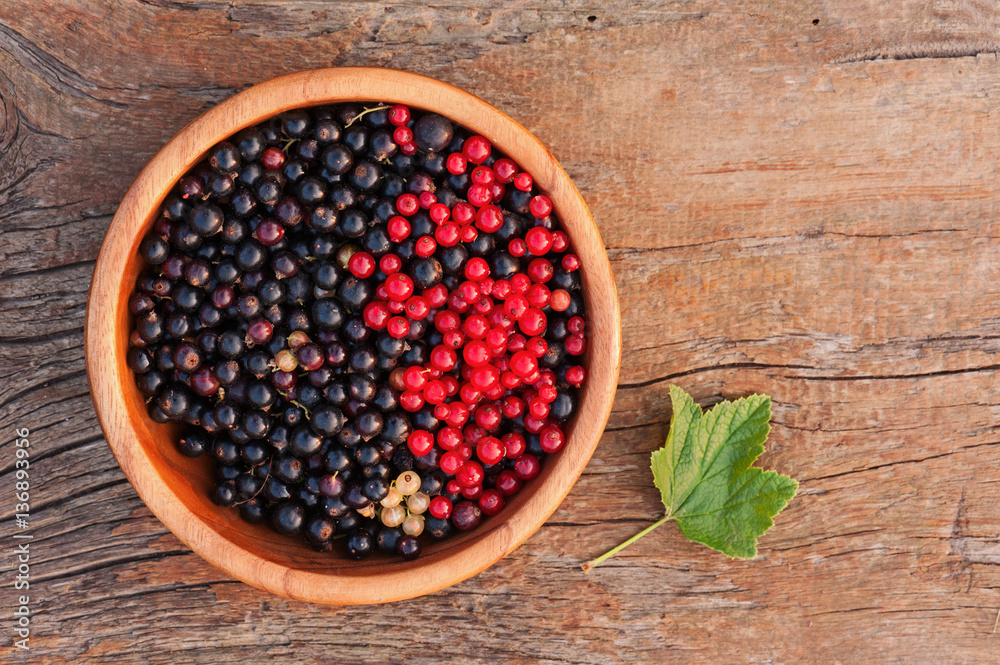 Sweet, black and red currant and green leaves in wooden bowl. Closeup. Selective focus. Sweet, black and red currant and green leaves in wooden bowl. Closeup. Selective focus.