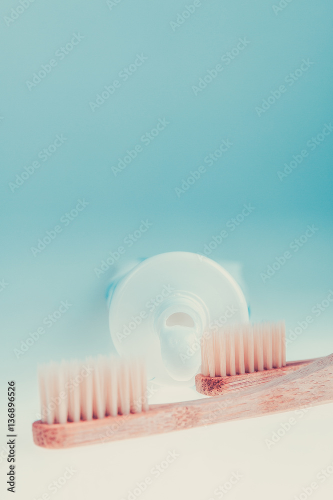Two beige dental brushes near tube of toothpaste on blue white background. Isolated. Toned photo. Two beige dental brushes near tube of toothpaste on blue white background. Isolated. Toned photo.