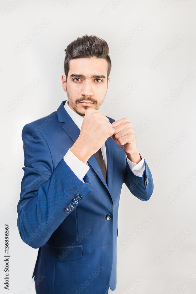 Young attractive man in a blue suit standing in a fighting stance on a gray background. Isolated Young attractive man in a blue suit standing in a fighting stance on a gray background. Isolated