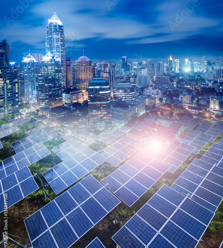 Solar Panels (solar cell) in solar farm and  The Modern City panorama  background at night.