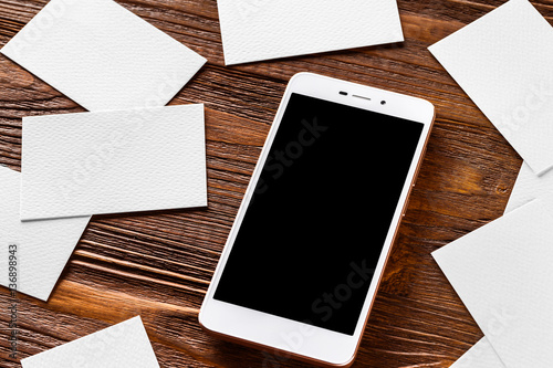 Mockup of cellphone and scattered business cards at brown wooden