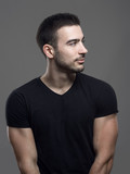 Profile view of happy confident young fit man in blank black shirt looking away over gray studio background. 