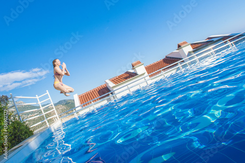 Woman in swimsuit jumping into swimming pool in the lotus position