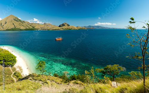 Komodo Coral Bay Viewpoint. View over white sand beach and coral bay at Komodo, Flores Indonesia. Grass in the foreground and mountains in the background.