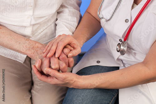 nurse with a stethoscope lovingly holds the hands of an elderly woman