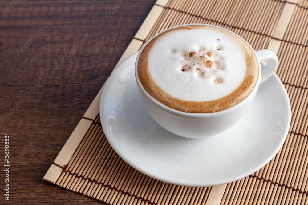 Coffee cup of cappuccino on bamboo mat, on wooden background wit