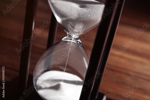 Time passing concept. Black hourglass with white sand on wooden background