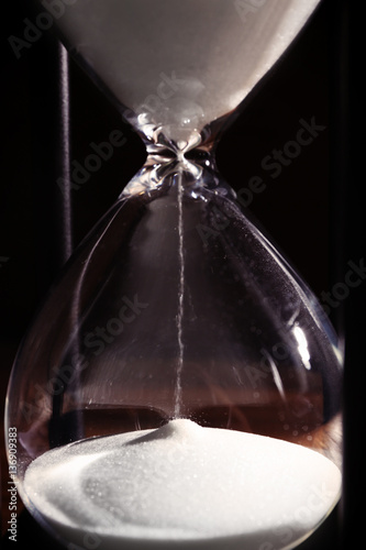 Time passing concept. Black hourglass with white sand, close up