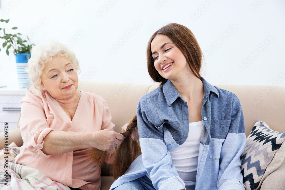 Grandmother pigtails braiding granddaughter's hair on couch at home Grandmother pigtails braiding granddaughter's hair on couch at home