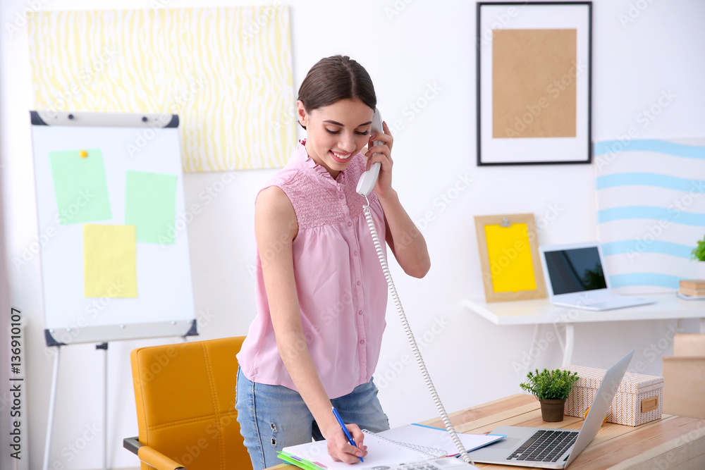 Beautiful young woman talking by telephone while working in office