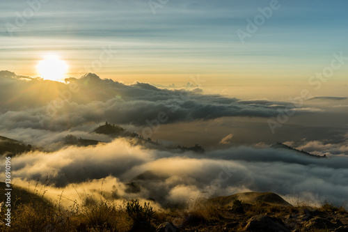 Mount Rinjani Cloudy Sunset View. View down the outside ridge of Gunung RInjani Volcano Crater, Lombok Indonesia. Sun is shining through the clouds, grassy mountain ridge.