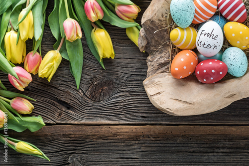 Osternest mit bunten Eier und Tulpen auf altem Holz