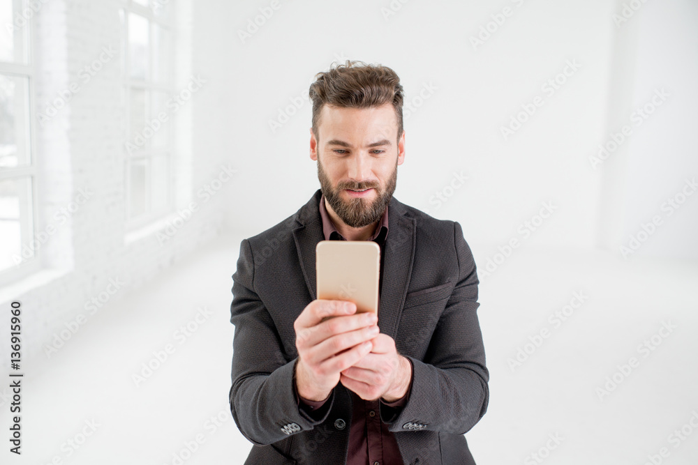 Elegant businessman in the dark suit using phone in the white office interior Elegant businessman in the dark suit using phone in the white office interior