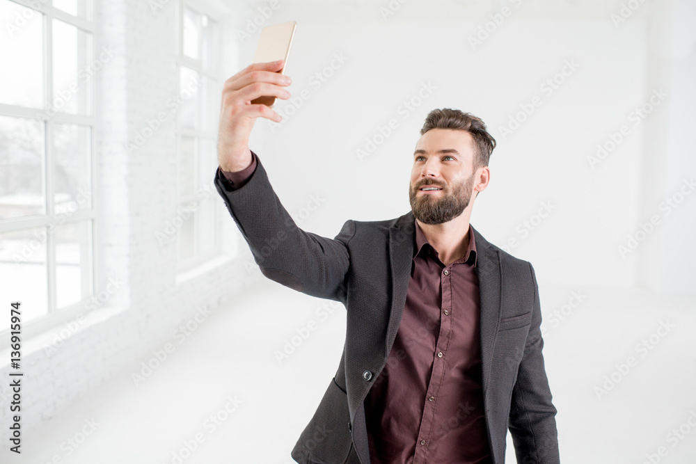 Businessman making self portrait with phone in the white office interior Businessman making self portrait with phone in the white office interior