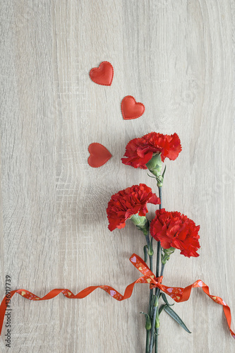 Red Carnations with ribbon and hearts on a wooden background. photo