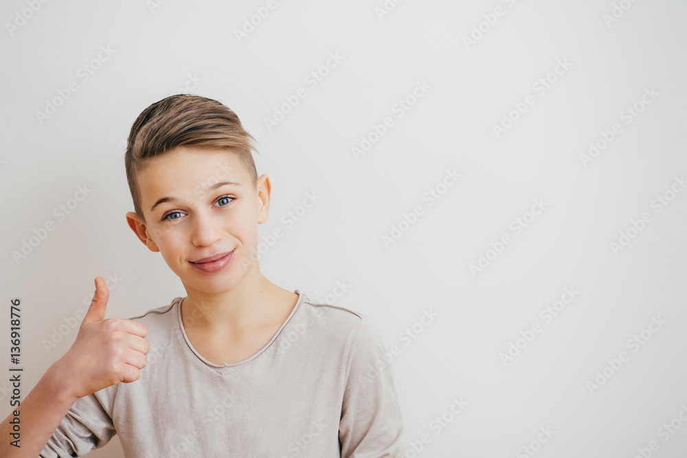 Portrait of a teenager boy giving a thumbs up sign on a light background