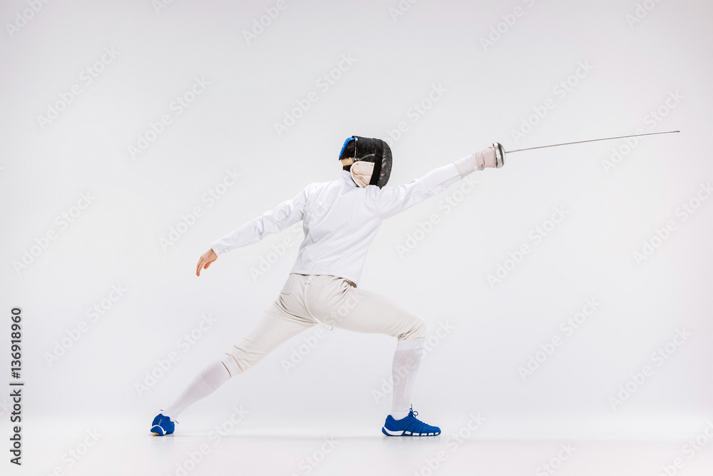 Man wearing fencing suit practicing with sword against gray Man wearing fencing suit practicing with sword against gray