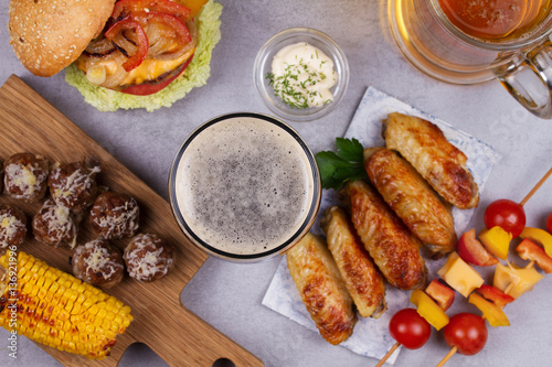 Glasses of beer with chicken wings, burger, meat balls, grilled corn and vegetables. Beer bites. Ale and food still life. View from above, top studio shot