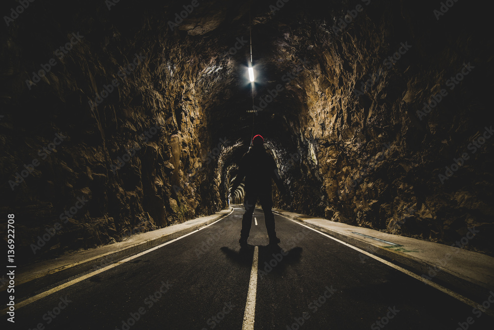 man standing at the entrance of an illuminated tunnel - outdoor activity
