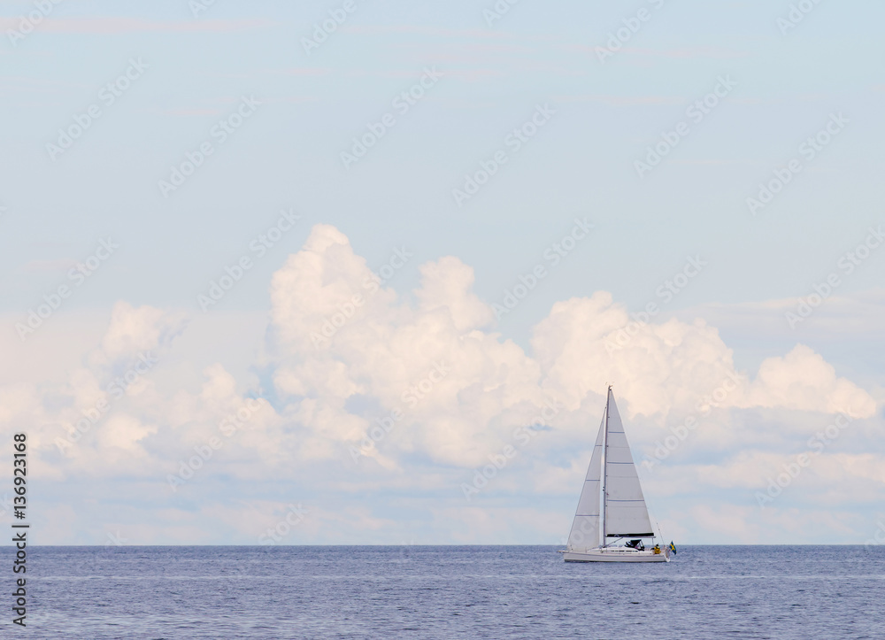 Sailboat on the glittering blue sea, large clouds
