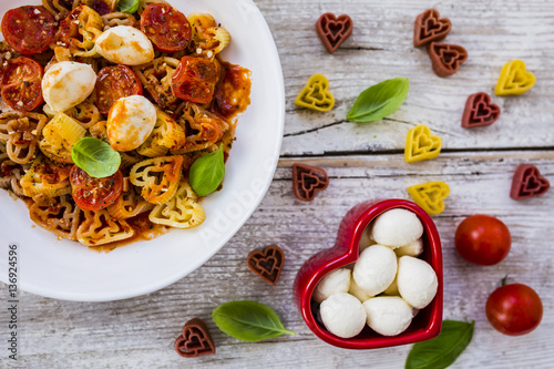 Heart-shaped pasta with tomatoes and basil on wooden background. Italian food on Valentine's Day. 