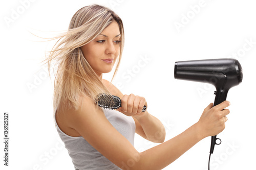 Pretty young woman using a hairbrush and a hairdryer