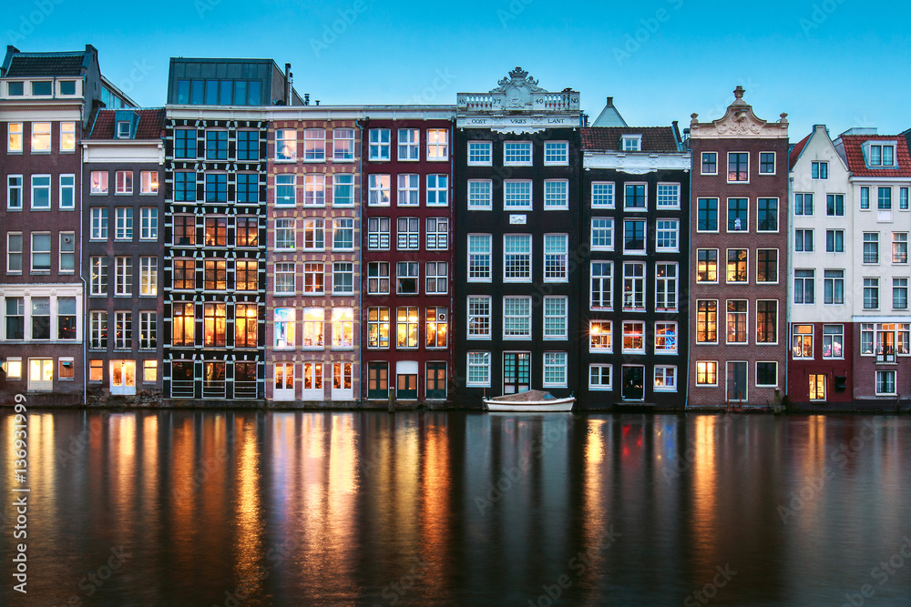 Famous old buildings with lights in Amsterdam reflecting in water as blue hour