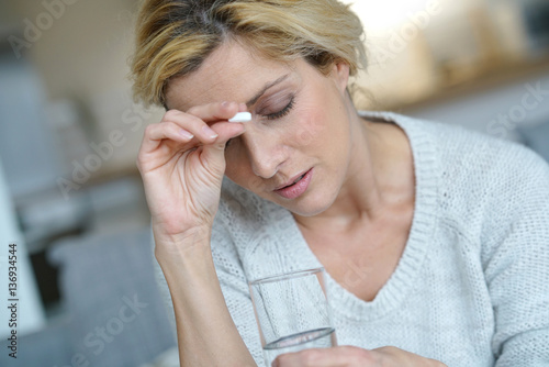 Canvas Print Middle-aged woman at home taking pill to ease headache