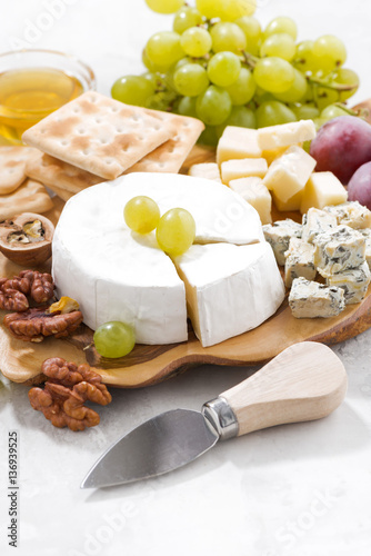 camembert, grapes and crackers on a white table, vertical