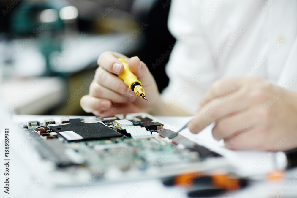 Fototapeta premium Closeup shot of unrecognizable man assembling circuit board using screwdriver and different tools on table in workshop