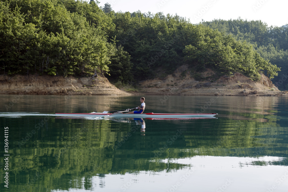 A Young single scull rowing competitor paddles on the tranquil lake