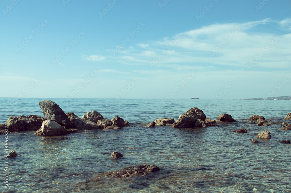 Serene seascape with rocks in the foreground and boat on horizon