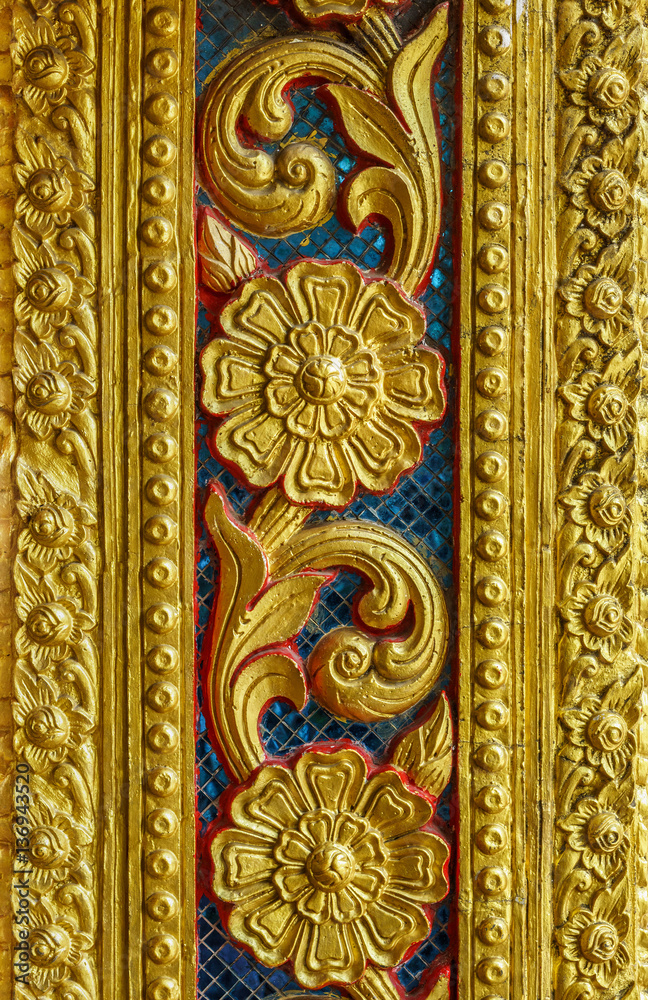 Vintage old golden floral sculpture on wall. The Thai design patterns are made from concrete and stucco.