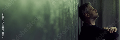 Fotografie Lonely man sitting against wall