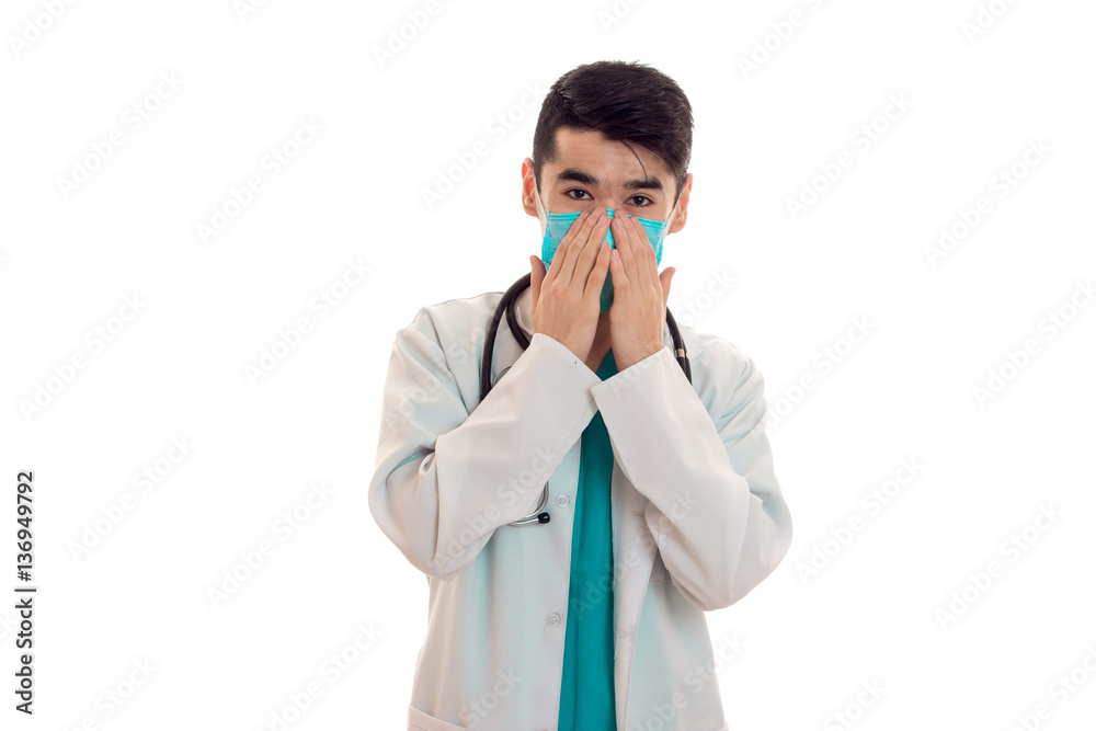 beauty young brunette male doctor with stethoscope in uniform and mask looking at the camera isolated on white background beauty young brunette male doctor with stethoscope in uniform and mask looking at the camera isolated on white background