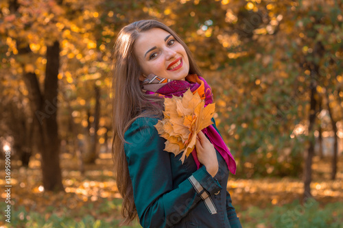joyful young girl stands smiling in the Park and keeps the leaves