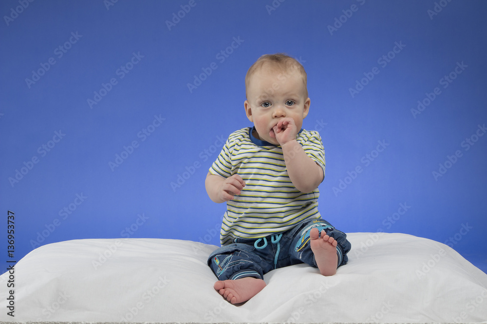 Fototapeta premium Adorable little baby boy, sitting on the white blanket, studio shot, isolated on blue background