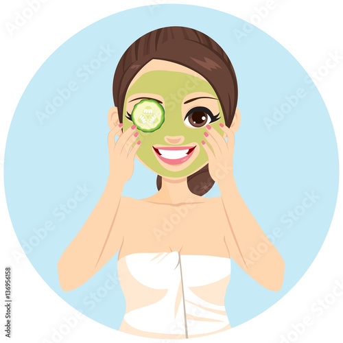 Beautiful brunette woman with applying cucumber slices on her green mud cleansing spa treatment