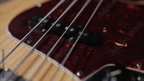 Vintage bass guitar in light wooden color. With red pickguard and two single pickups. Silver bridge. Close-up smooth motion.