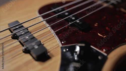 Vintage bass guitar in light wooden color. With red pickguard and two single pickups. Silver bridge. Close-up smooth motion.