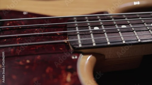 Vintage bass guitar in light wooden color. With red pickguard and two single pickups. Silver bridge. Close-up smooth motion.