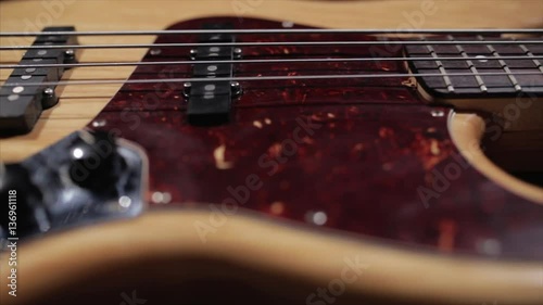 Vintage bass guitar in light wooden color. With red pickguard and two single pickups. Silver bridge. Close-up smooth motion.