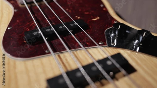 Vintage bass guitar in light wooden color. With red pickguard and two single pickups. Silver bridge. Close-up smooth motion.