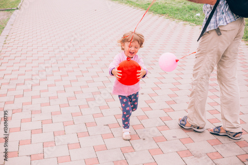 Happy little girl playing with colorful toy balloons outdoors.