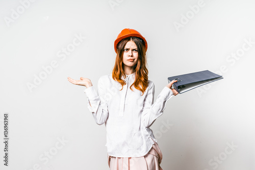 Young engineer with pensive face and security helmet isolated over white background question.Girl don`t understand in buildings.Woman questioned,raised arms photo