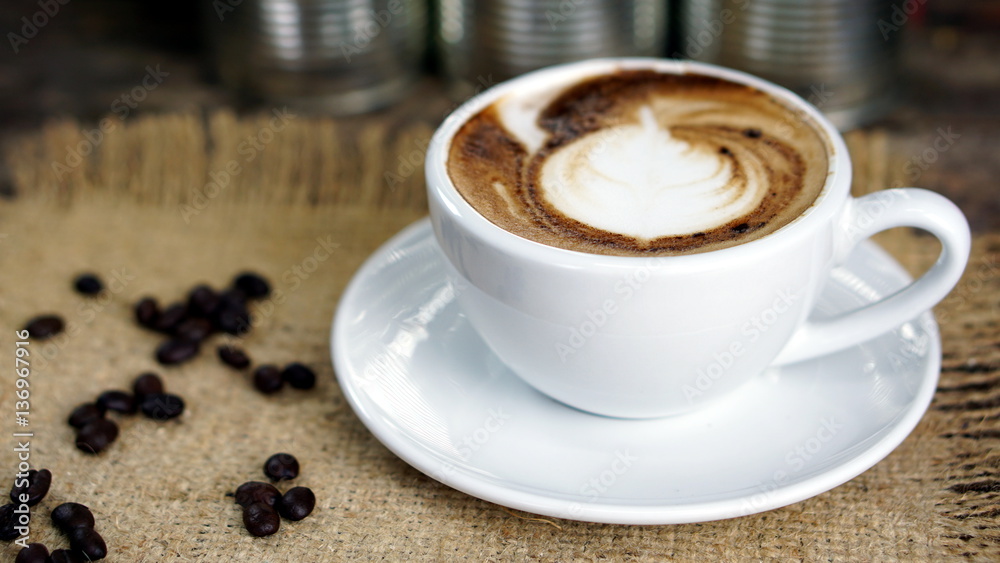 Cappuccino coffee. A cup of latte, cappuccino or espresso coffee with milk put on a wood table with dark roasting coffee beans. Drawing the foam milk on top. Cappuccino coffee. A cup of latte, cappuccino or espresso coffee with milk put on a wood table with dark roasting coffee beans. Drawing the foam milk on top.