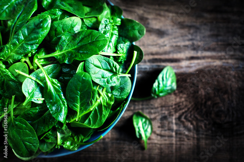 Fresh green baby spinach leaves  in a bowl on a rustic wooden ta photo