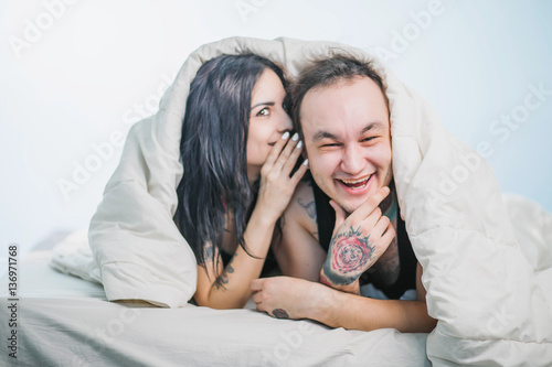 the guy with the girl in the tattoo bed whispering in ears laughs fun under the covers